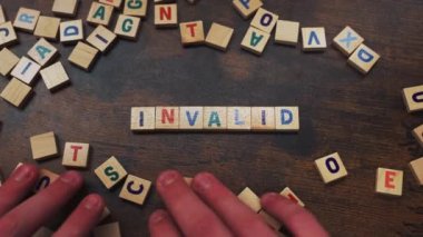 Symbolic concept represented by the wordplay INVALID. Numerous square wooden puzzles with colourful letters on them placed on a dark wooden table. . High quality 4k footage