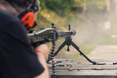 08.07.2022 Warsaw, Poland Unrecognizable caucasian person in red protective earphones shooting with machine gun. Competition at shooting range. Firearm concept. High quality photo