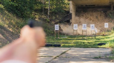Two blurred hands of an unrecognizable caucasian person aiming at paper targets with a black gun. Outdoor gun range. Firearm concept. High quality photo