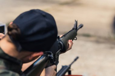 08.07.2022 Warsaw, Poland Unrecognizable caucasian person in a black baseball hat using brand-new M16 rifle. Blurred background. Outdoor shooting range. High quality photo