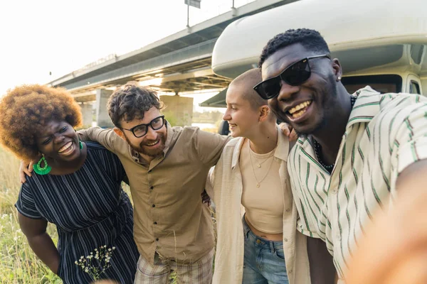 Interracial friendship. Group of happy close friends, reunited on their camping van trip, traveling through the country. Laughing and taking selfies together near the river. High quality photo