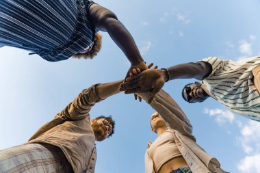 Multicultural group of young people standing in circle and holding their hands on top of each other. Unity, teamwork and support concept. High quality photo