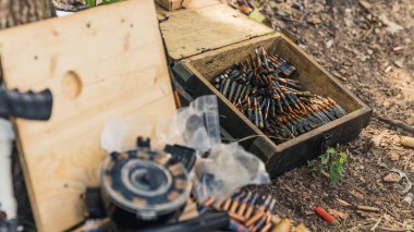 Outdoor shot focused on the background where is big wooden box full of black riffle bullets. Ammunition concept. Day at the shooting range. High quality photo