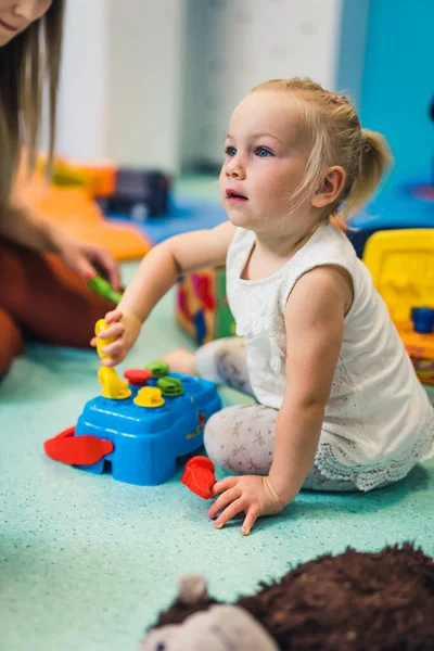 Caucasian toddler girl playing with a colorful plastic shape sorter toy and building blocks. Work on problem-solving skills, fine motor and gross motor skills development through sensory play at the