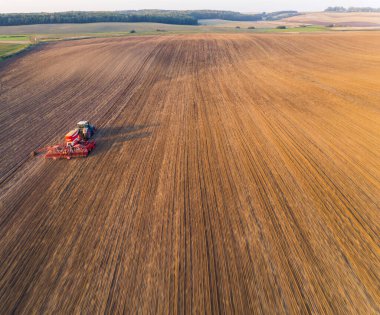 Bue tractor driving through vast golden-brown field and green farmland in the background. Sowing machine. Horizontal shot. High quality photo