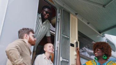 A multicultural group of college friends standing near their motorhome and talking, laughing, enjoying spending time together camping in nature . High quality 4k footage