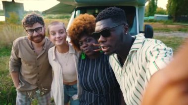 Interracial friendship. Group of four close friends taking a selfie on a smartphone together near the river bridge. Reunited on their camping van trip, traveling through the country. . High quality 4k