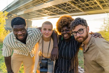 Multi-ethnic group of best old friends, who finally reunited after a long time separate living and studying in different countries, having a weekend picnic near the river. Taking pictures together