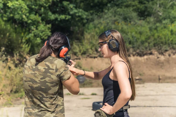 Shooting with the instructor. Outdoor shooting range. Long-haired female caucasian instructor teaching a black-haired muscular man in a moro t-shirt how to use a weapon. High quality photo