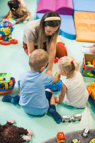 Learning through play at the nursery school. Caucasian toddlers and their teacher playing with colorful plastic playhouses, building blocks, cars and boats. Imagination, creativity, fine motor and