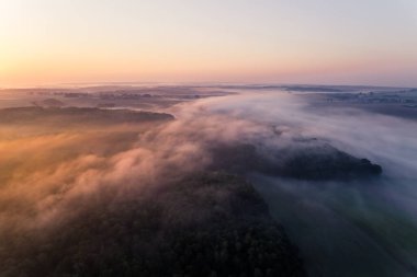 Thick fog spreading over forest and farm fields during colorful sunrise. Orange glare. Landcape of Roztocze Poland. Horizontal shot. High quality photo