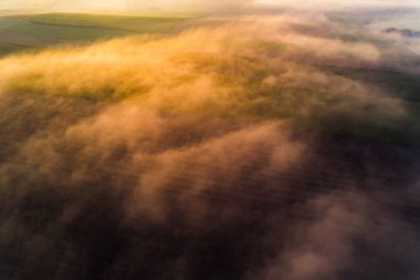 Thick fog covering colorful farm fields with orange glaze from rising sun. Morning landscape of Roztocze Poland. Birdseye view. Horizontal shot. High quality photo