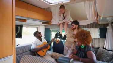 Interracial group of four good friends on a summer road traveling, sitting inside their comfortable modern motorhome, chatting and relaxing. RVs interior. High quality 4k footage