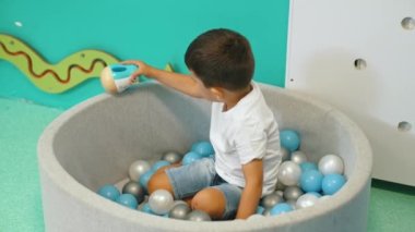 Toddler boy playing with a toy while sitting in a ball pit full of colorful balls. A ball pit - a great place for kids to jump, crash, and wiggle. Sensory play at the nursery school. . High quality 4k