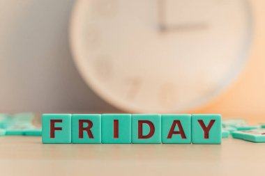The word FRIDAY made of square colorful letters on the table with a time clock on the background. Happy end of the working week. High quality photo