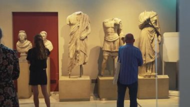 07.13.2022 Thessaloniki, Greece. Wide indoor shot of two tourists visiting one of the rooms of the Archeological Museum of Thessaloniki. Old white statues. High quality 4k footage