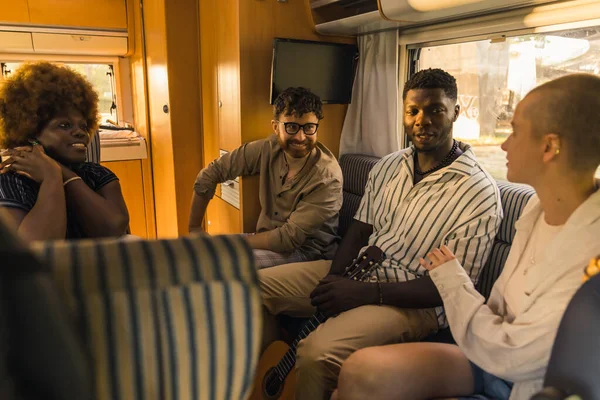 Interracial group of four good friends on a summer road traveling, sitting inside their comfortable modern motorhome, chatting and relaxing. RVs interior. High quality photo