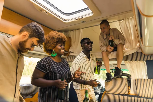 Interracial group of close friends dancing to the music inside their comfortable spacious motorhome and drinking beer. Celebrating a birthday on a camping van trip during summer. High quality photo