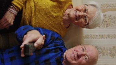 vertical video of a very cute senior couple watching TV, medium shot home senior people support concept. High quality 4k footage