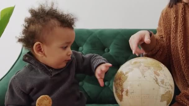 Cute Little Boy Holding Cookie Spinning Globe Medium Shot Home — Αρχείο Βίντεο