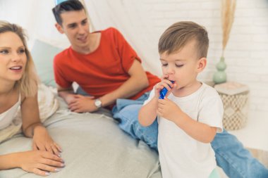 Party horn experience for the first time in life. Young caucasian couple watching their son trying to blow dark blue party horn. Birthday concept. High quality photo