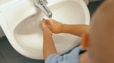 Toddler boy washing his hands with soap after playtime at the nursery school. Concept of early healthy hygiene learning for kids wellness. High quality 4k footage