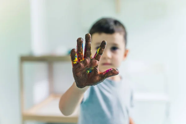 Cling film painting. Toddlers painting with a sponge, brushes and paints on a cling film wrapped all the way round the wooden shelf unit. A teacher helping them. Creative activity for kids sensory