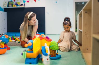 Playtime at nursery school. Toddler girl with a teacher sitting on the floor and playing with building blocks, colorful cars and other toys. imaginative play. High quality photo