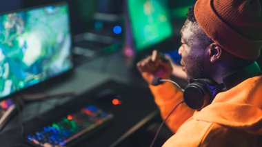 Teenager in orange clothes wearing headphones around his neck playing online game celebrating success. Blurred background. High quality photo