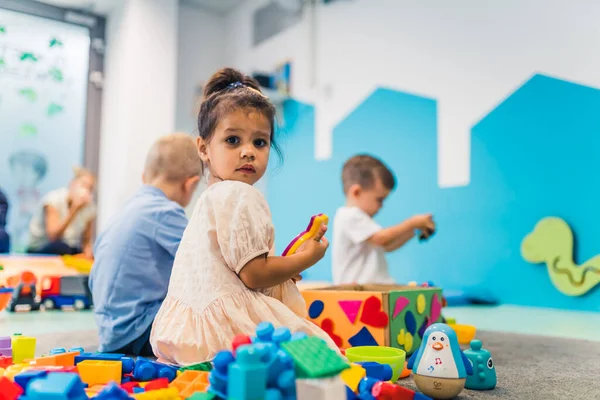 Playtime at nursery school. Toddlers sitting on the floor and playing with building blocks, colorful cars and other toys. How to interact with others and develop critical lifelong skills. High quality