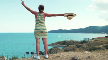 Çizgili elbiseli neşeli beyaz kadın kollarını uzatırken güzel Yunan deniz manzarasına hayranlık duyuyor. Tatil konsepti. Yüksek kalite 4k görüntü