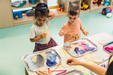 Multi-cultural nursery school. Toddlers playing with striped straws and milk painting, using nontoxic food coloring for colors. Creative kids activity for using their senses and brain development