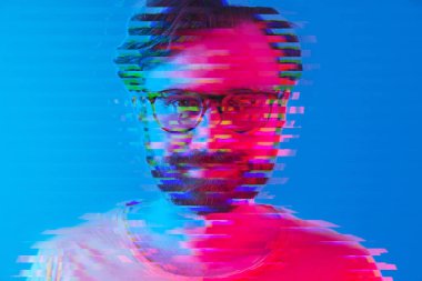 Kameraya bakan siyah gözlüklü ve turuncu tişörtlü, kalın saçlı, orta yaşlı Avrupalı esmer bir adamın yakın plan çizimi. Arıza etkisi. Mavi arka plan. Yüksek kalite fotoğraf