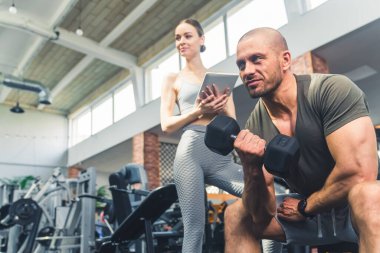 Genç bir bayana spor salonundaki dambıllarla nasıl egzersiz yapılacağını gösteren bir eğitmen. Yüksek kalite fotoğraf