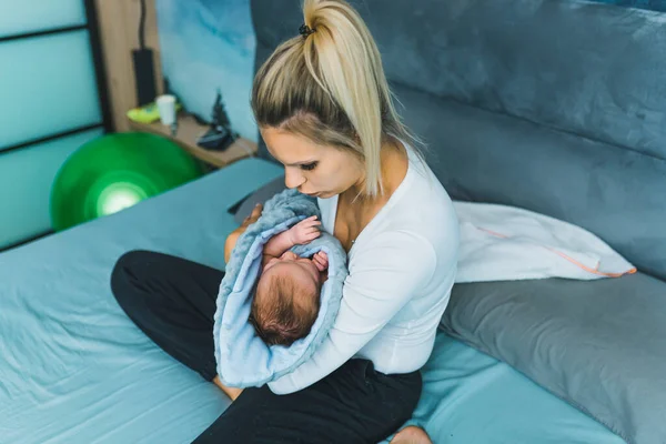 Pretty caucasian married woman holding a newborn baby boy in her arms, putting him to sleep in a bedroom. High quality photo
