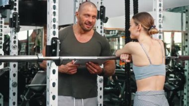 Spor salonundaki halterde dinlenen beyaz kadın müşteriye egzersiz planını açıklamak için tablet kullanan beyaz kaslı kel erkek antrenör. Yatay video. Yüksek kalite 4k görüntü