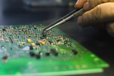 PCB baskılı devre kartının yakın çekim görüntüsü, monte edilmiş elektrik bileşenleri ve parçaları değiştiren cımbızla el. Elektronik tamir. Hassasiyet ve odaklanma. Yatay çekim. Yüksek kalite fotoğraf