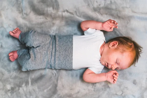 一个婴儿 棕色的秀发 躺在床上 仰卧在灰色的毛毯上 胳膊翘起 高质量的照片 — 图库照片