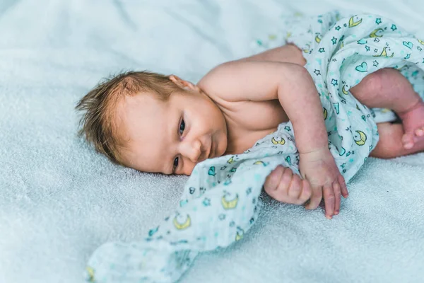 New life. Cute caucasian sleepy baby boy partially covered with soft blanket lying down on bed covered with baby blue sheets. . High quality photo