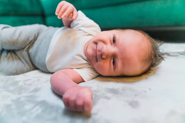 一个有着一头可爱棕色头发的男婴躺在地板上的灰色毯子上 对着摄像机笑着 高质量的照片 — 图库照片