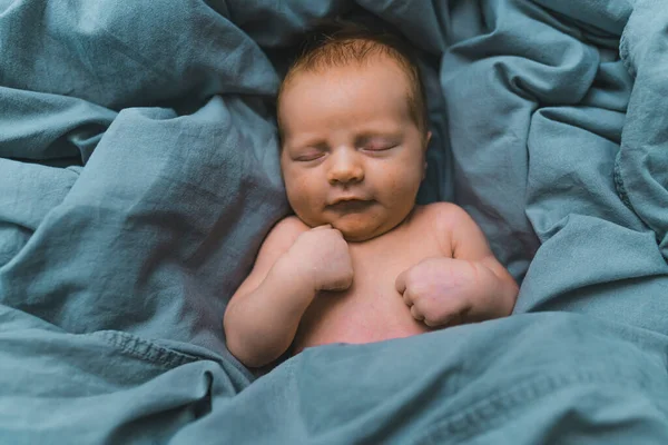 Closeup portrait of an adorable young infant baby boy lying on bed covered with dark blue bed sheets. New life. High quality photo