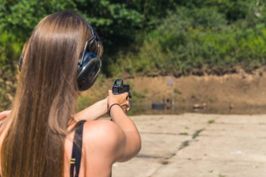 Güneşli bir günde atış poligonunda uzun saçlı bir kızın silahla bir hedefi vuruşunun arkası. Yüksek kalite fotoğraf