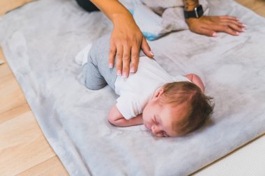 Beyaz tişörtlü, gri eşofmanlı, göbeğinde açık gri bebek minderinin üstünde yatan küçük bebek bebek. Tanımlanamayan beyaz bir ebeveyn yeni doğan bebeğe sırt masajı yapıyor. Yüksek kalite fotoğraf