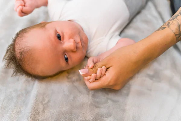 New family member. Closeup indoor shot of a dark-haired and dark-eyed caucasian baby boy touching his mothers thumb with all of his little hand. Parent-child relationship. High quality photo