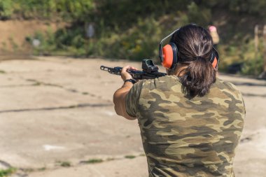 Atış poligonuna nişan alan ve siyah bir tüfekle orta mesafeden ateş eden bir adamın arka görüntüsü. Yüksek kalite fotoğraf
