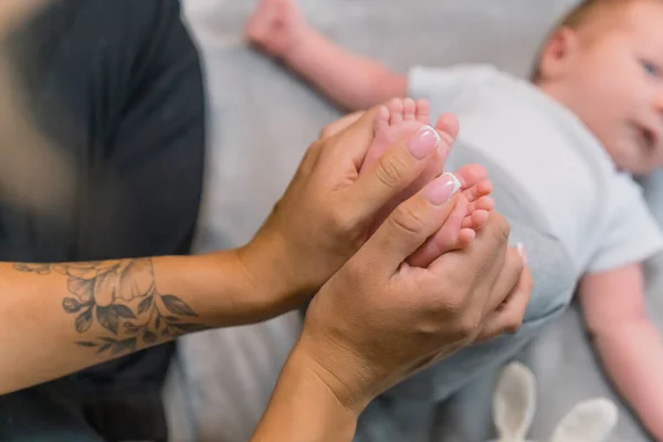 Feet massage for little babies. Relaxation at home. Tattooed hands of a caucasian mother giving a foot massage to her adorable little infant baby boy. Child blurred in the background. High quality