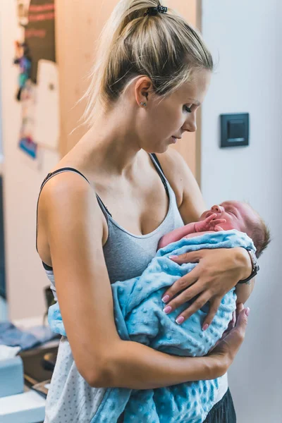 New family member. Motherhood concept. Vertical indoor shot of a young millennial skinny caucasian girl holding her adorable infant baby boy. Accessories for newborns - blanket. High quality photo