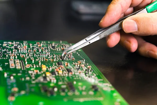 Karmaşık devre kartının elektrik bileşenlerini değiştiren gümüş cımbızlarla yakın çekim. Modern teknoloji. Elle tamir ediliyor. Yatay çekim. Yüksek kalite fotoğraf