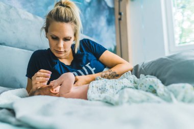 Yatak odasında uzanmış sarı saçlı beyaz bir kadın. Küçük oğlu ona sevgiyle dokunuyor. Şefkatli anne. Kapalı alanda yatay çekim. Yüksek kalite fotoğraf