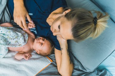 Genç beyaz sarışın anne yeni doğmuş bebeğine sarılıp onun eline dokunuyor. Annelik. Sakin ve rahat ol. Kapalı alanda yatay çekim. Yüksek kalite fotoğraf